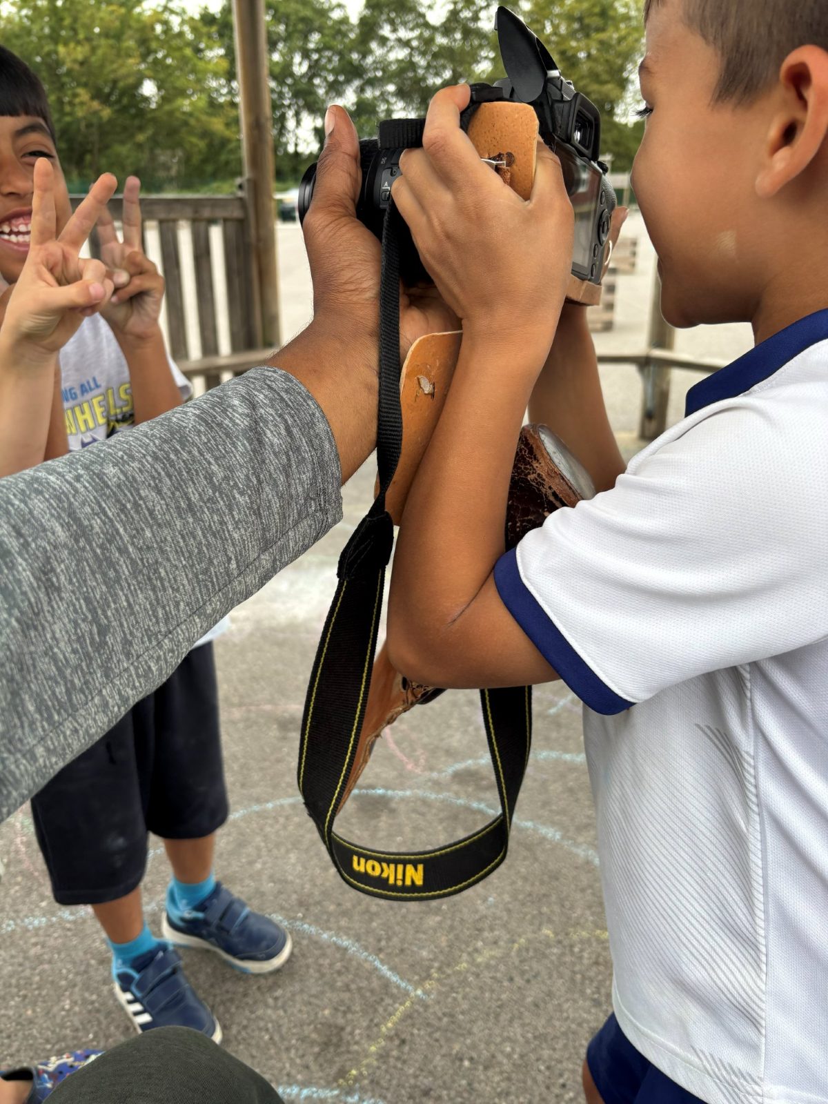 A child at camp using a camera while another pulls a face behind them